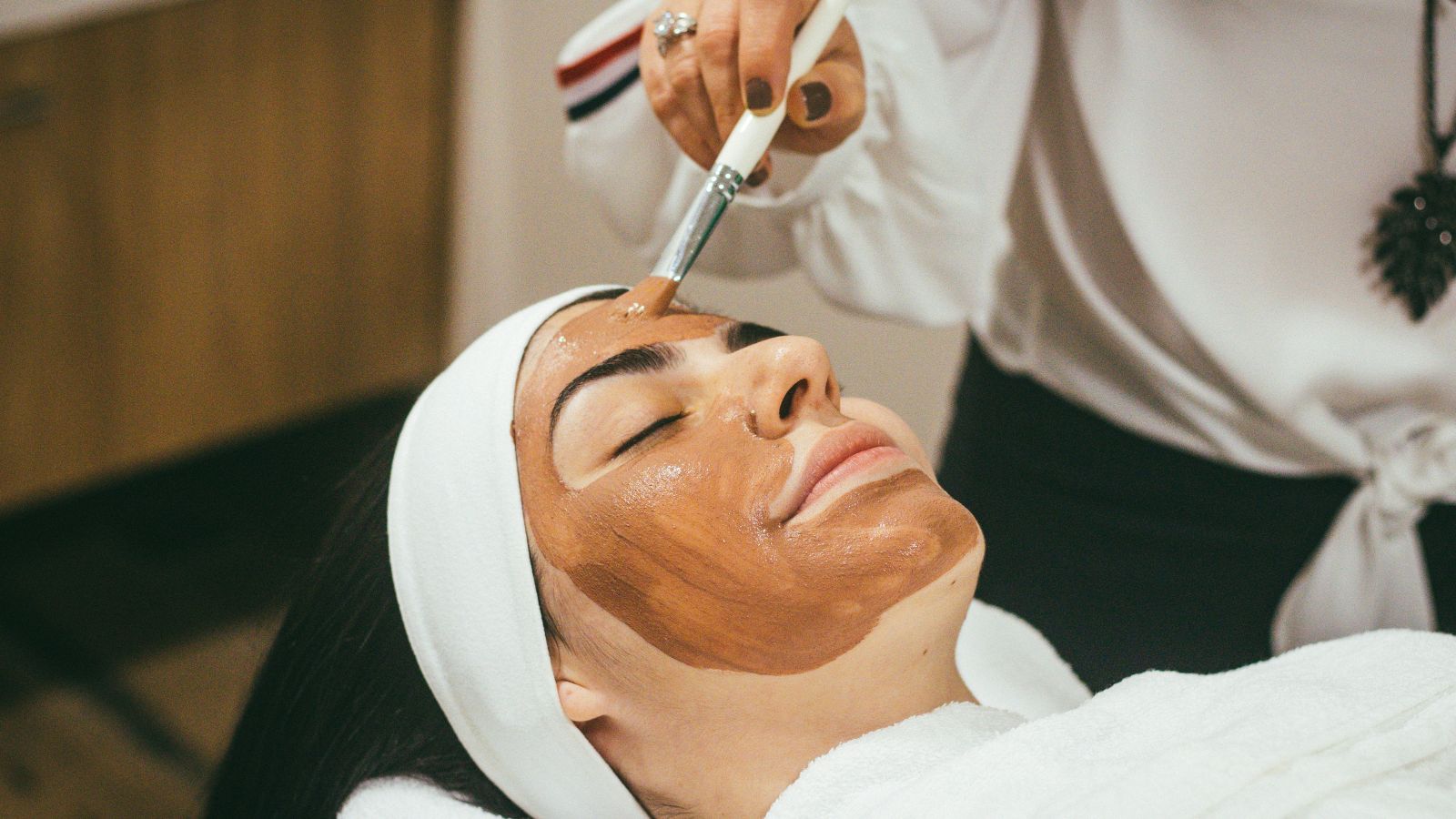 6X Bookings Boost for a Spa Business 19 A person is lying down with a white headband and towel while another person applies a brown facial mask on their face using a brush. The serene spa setting reflects the ultimate relaxation similar to how targeted google ads can enhance ROI for 6X Bookings Boost for a Spa Business