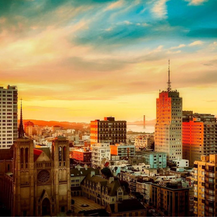 A vibrant cityscape during sunset with a variety of buildings, including a prominent cathedral in the foreground. The sky displays an array of warm colors, and in the background, a bridge spans over a body of water, creating an enchanting view that could enhance ROI for tourism investments. it used for 220% Organic Traffic Growth for Real Estate Firm casestudy at Enhance ROI featured iamge